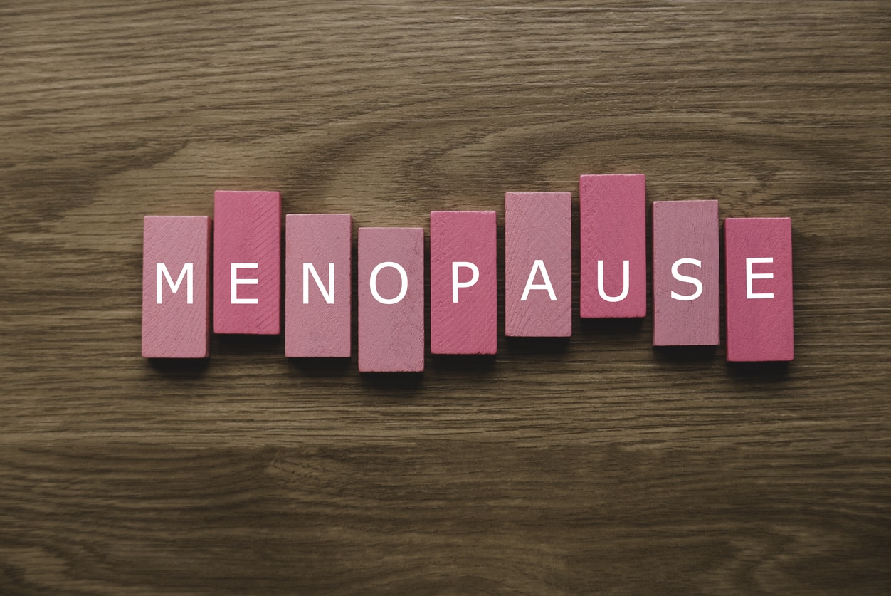 a pink wooden block with a text of menopause on wooden background.