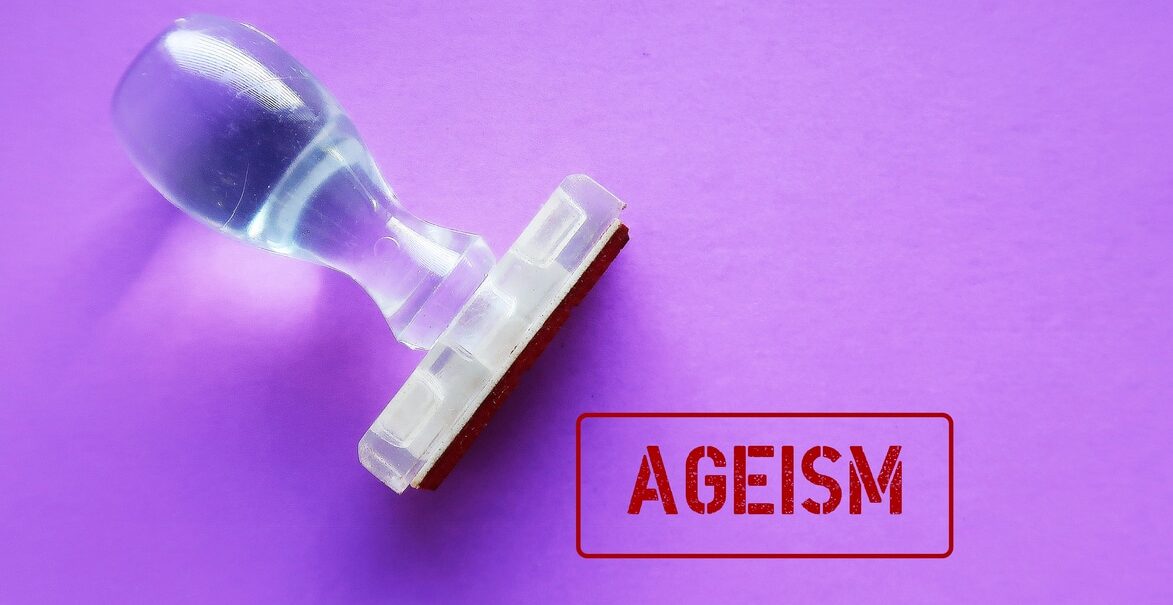 rubber stamp on purple background with stamp text ageism, means when age is used to categorize and divide people that lead to harm, disadvantage, and injustice stereotypes of prejudice discrimination by age