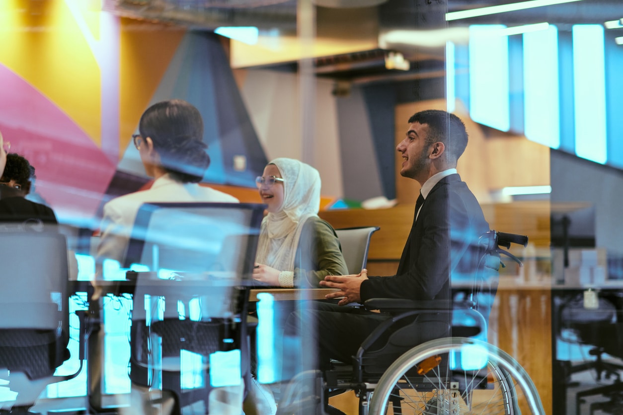 in a modern glass startup office, a wheelchair bound director leads a successful meeting with colleagues, embodying inclusivity and teamwork.