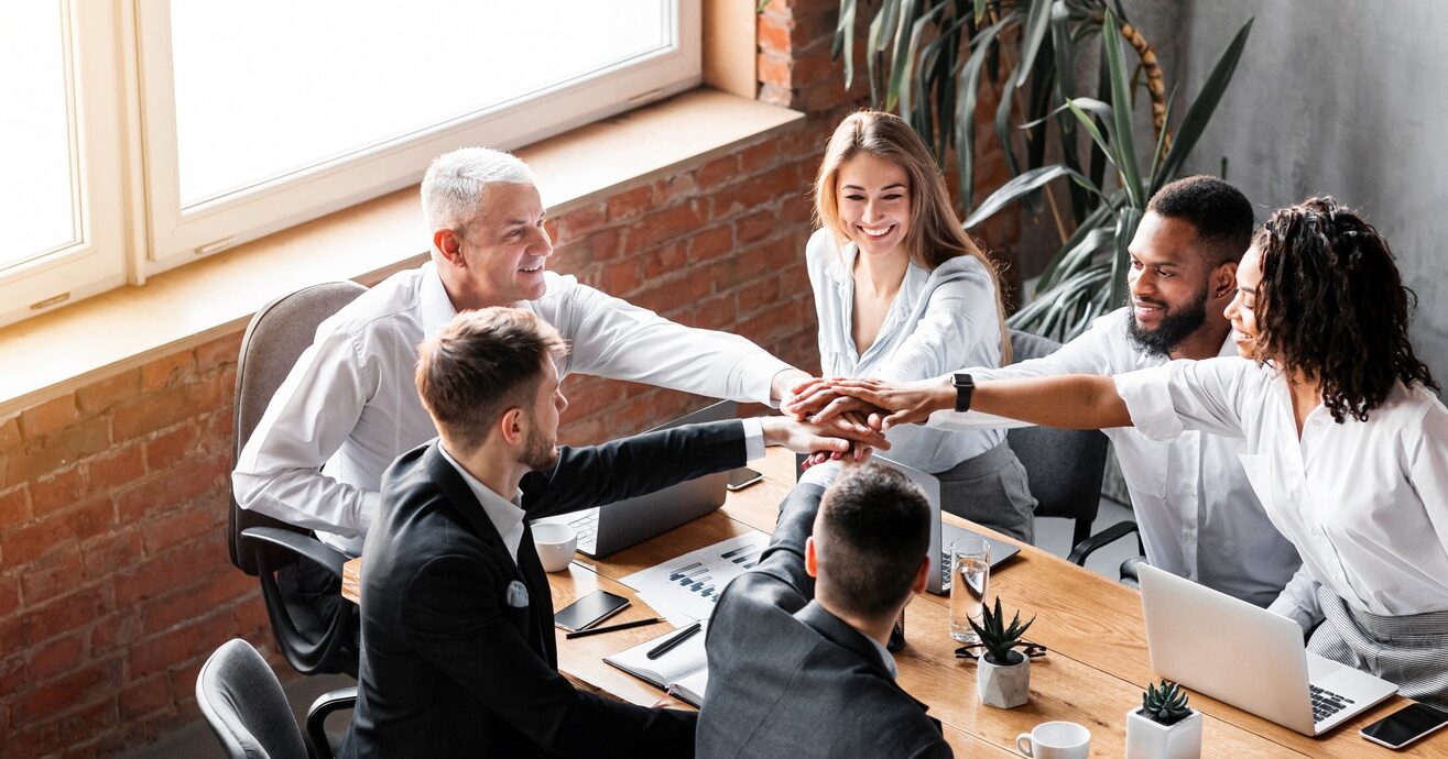 united business team holding hands sitting together in modern office